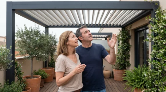 Dos adultos españoles discutiendo ajustes de lamas bajo pérgola bioclimática de aluminio